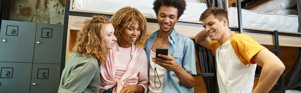 Joyful african american man browsing internet on smartphone near friends in hostel, banner — Stock Photo