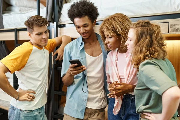 Youthful african american man using smartphone near multicultural buddies in students hostel — Stock Photo