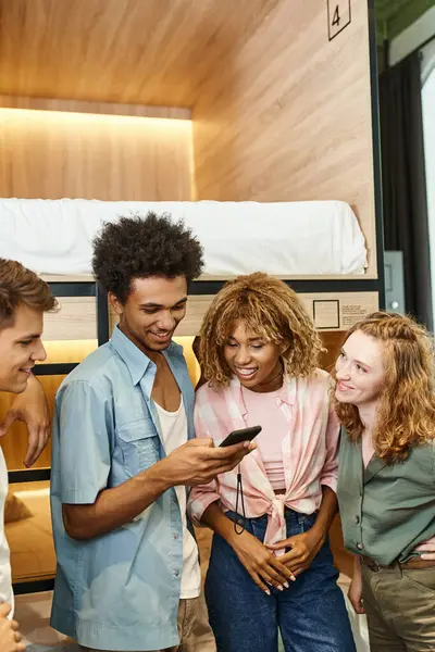 Happy african american student with mobile phone near interracial students in youth hostel — Stock Photo