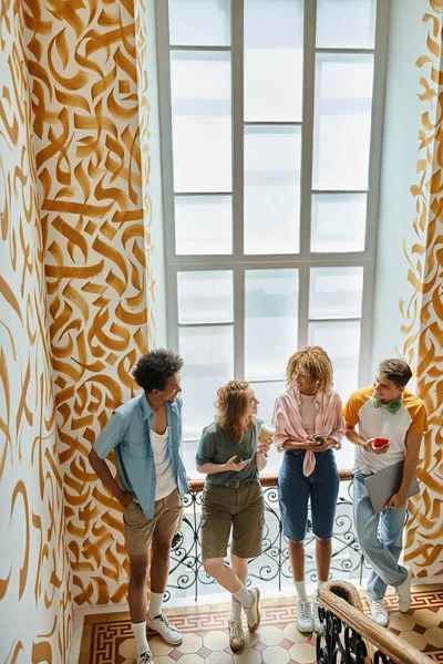 Amigos multiculturais alegres com gadgets falando em escadaria de estudantes modernos albergue — Fotografia de Stock