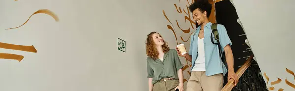 Carefree african american man with paper cup walking with girlfriend on staircase of hostel, banner — Stock Photo