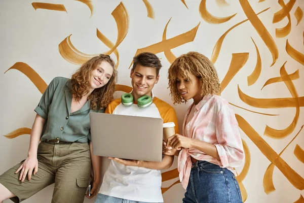 Souriant interracial femmes regardant ordinateur portable près étudiant sur escalier sur auberge contemporaine — Photo de stock