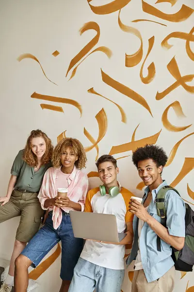 Junge multiethnische Freunde mit Coffee to go und Laptop, die im Treppenhaus des Hostels in die Kamera schauen — Stockfoto