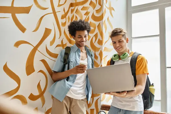Африканский американский студент с бумажной чашкой рядом улыбающийся друг с ноутбуком на лестнице общежития — стоковое фото