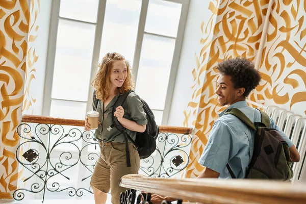 Happy and cheerful multiethnic students with backpacks walking on staircase of youth hostel — Stock Photo