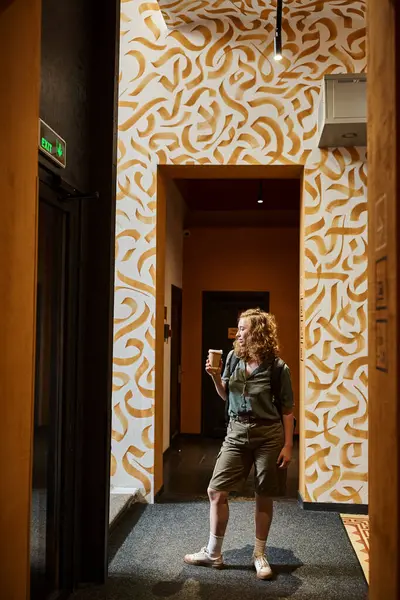 Junge Frau mit Kaffee to go im Flur mit bunten Wänden im Studentenwohnheim, Reisender — Stockfoto