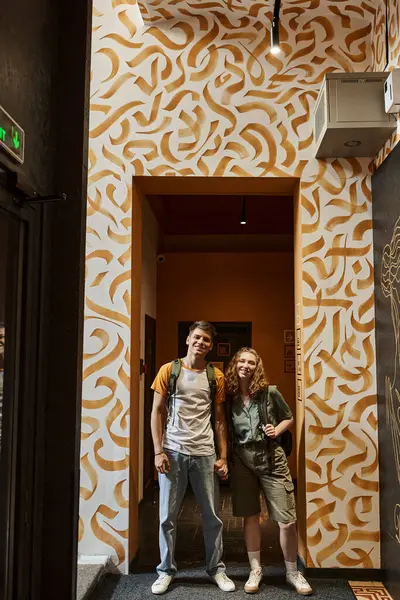Alegre joven pareja mirando a la cámara en el pasillo de los estudiantes albergue con diseño moderno, viajeros - foto de stock