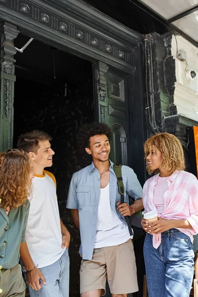 Joyful multicultural buddies talking near youth hostel on city street, friendship and travel — Stock Photo