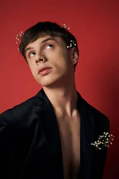 Good looking young man in velvet blazer with flowers in hair looking at camera on red background — Stock Photo