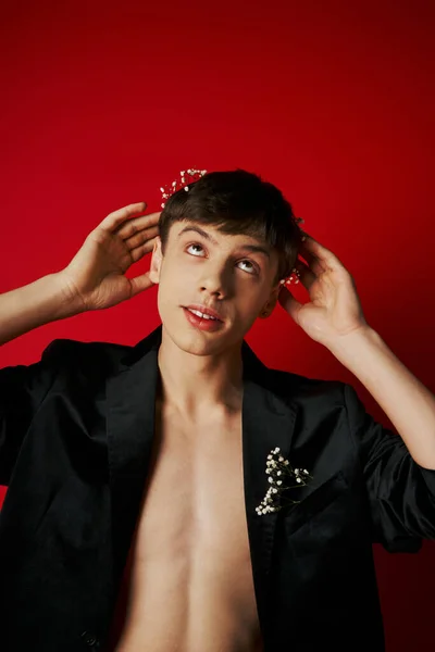 Bel homme en veste de velours élégant levant les yeux et mettant des fleurs dans les cheveux sur fond rouge — Photo de stock