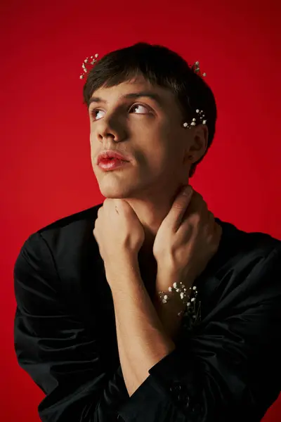 Dreamy young man in velvet blazer with flowers in hair looking up and touching neck on red backdrop — Stock Photo