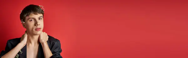 Young man in velvet blazer with flowers in hair looking at camera and touching neck on red, banner — Stock Photo