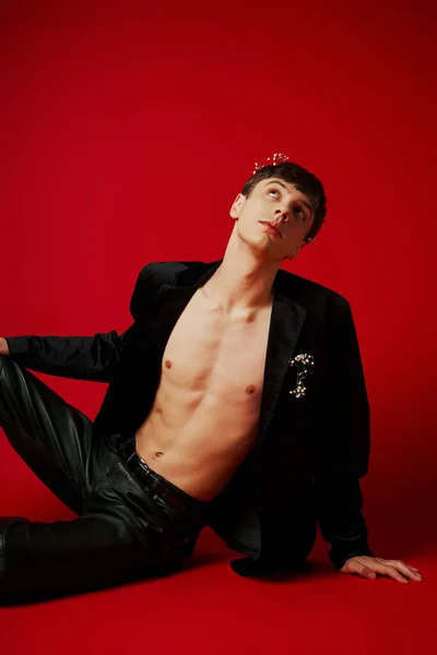 Dreamy and fashionable man in velvet jacket and leather pants looking up on red background — Stock Photo