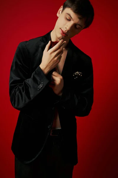 Romantic and dreamy young man in velvet jacket looking at rose in hands on red background — Stock Photo
