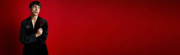Portrait of romantic young man holding rose in hand and looking away on red background, banner — Stock Photo