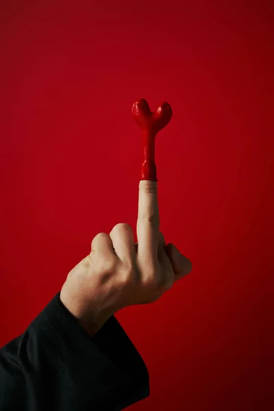 Обрезанный снимок провокационного мужчины, показывающего средний палец с воздушным шаром на красном фоне, 14 февраля — стоковое фото