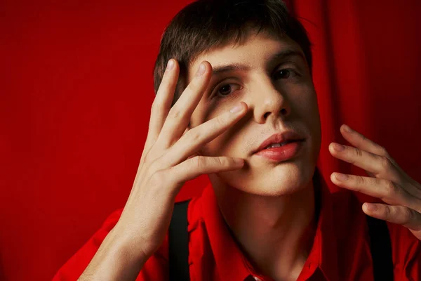 Close up shot, pensive young man in shirt and suspenders touching his face on red background — Stock Photo