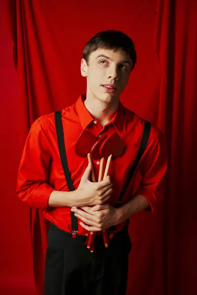 Dreamy cupid in shirt and suspenders holding heart shaped arrows on red background, 14 February — Stock Photo