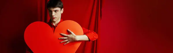 Young man in shirt embracing large heart shaped carton on red background, Valentines day banner — Stock Photo