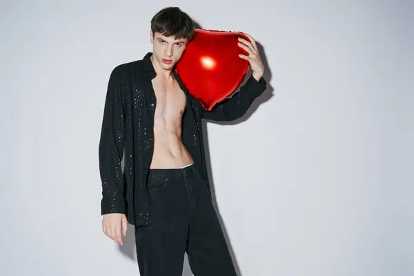 Stylish young man in black shiny open shirt holding red balloon on grey background, 14 February — Stock Photo