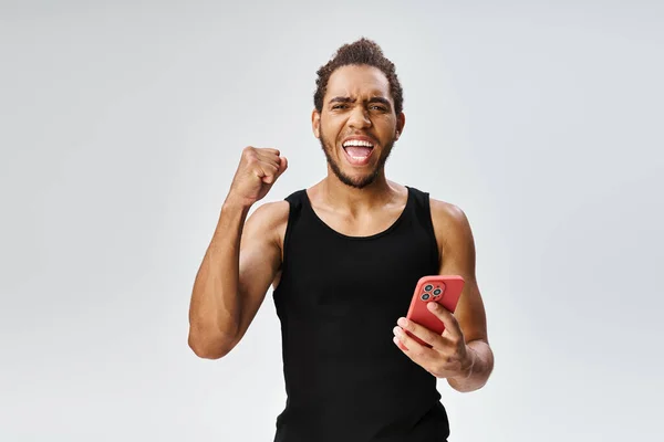 Веселий атлетичний афроамериканський спортсмен тримає телефон і дивиться на камеру, онлайн ставки — стокове фото