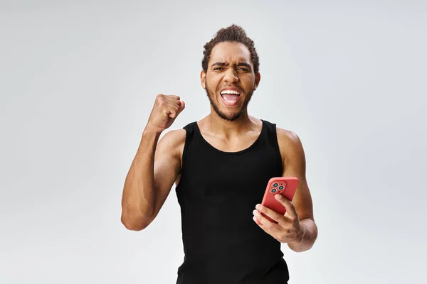 Cheerful athletic african american sportsman holding phone and looking at camera, online betting — Stock Photo