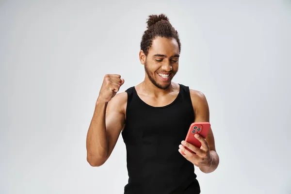 Alegre atlético afroamericano hombre en ropa deportiva mirando a su teléfono inteligente, apuestas en línea - foto de stock