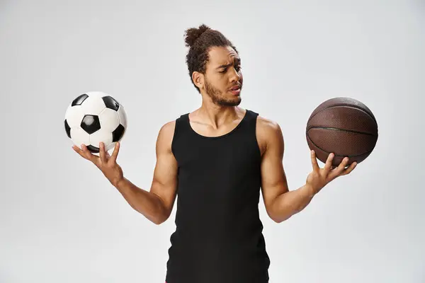 Sportif afro-américain confus posant avec le football et le basket-ball dans les mains sur fond gris — Photo de stock