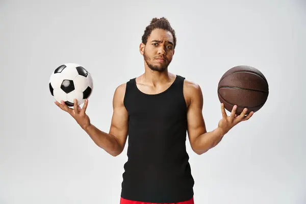Confused african american man in sportwear holding football and basketball and looking at camera — Stock Photo