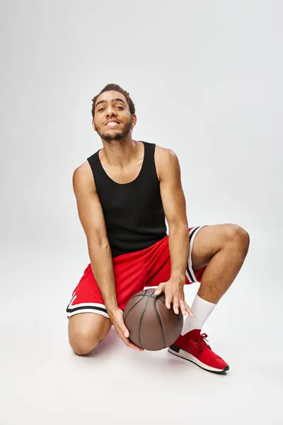 Homem americano africano alegre posando com seu basquete e sorrindo para a câmera em pano de fundo cinza — Fotografia de Stock