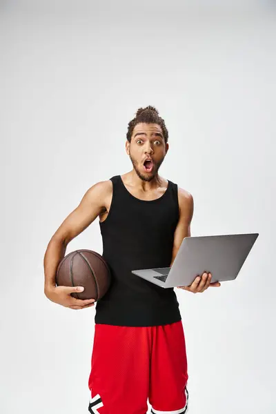 Sorpreso sportivo afroamericano in possesso di basket e laptop guardando la fotocamera, scommesse online — Foto stock