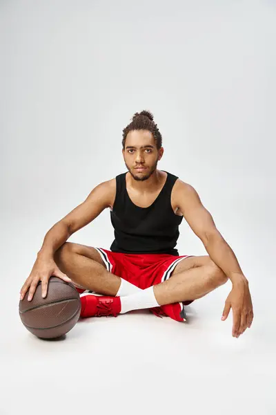 Handsome african american man in sportwear sitting with crossed legs on floor with basketball — Stock Photo