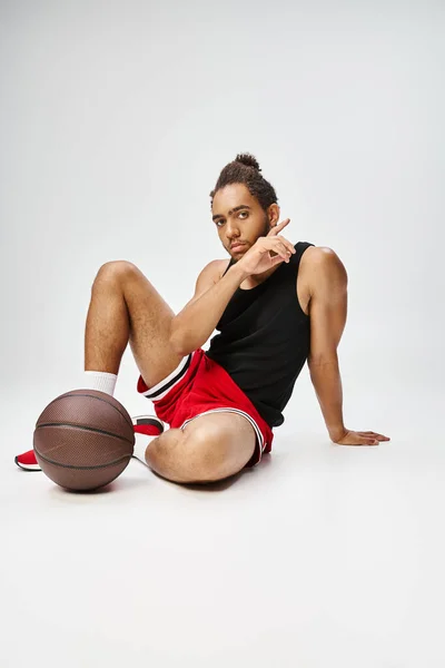 Attraente giovane uomo africano americano in comodo sportwear seduto accanto al basket sul pavimento — Foto stock