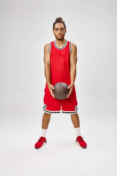 Homem americano africano bonito em sportwear vibrante segurando basquete e olhando para a câmera — Fotografia de Stock