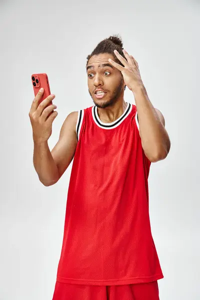 Shocked african american sportsman looking at his smartphone on gray backdrop, online betting — Stock Photo