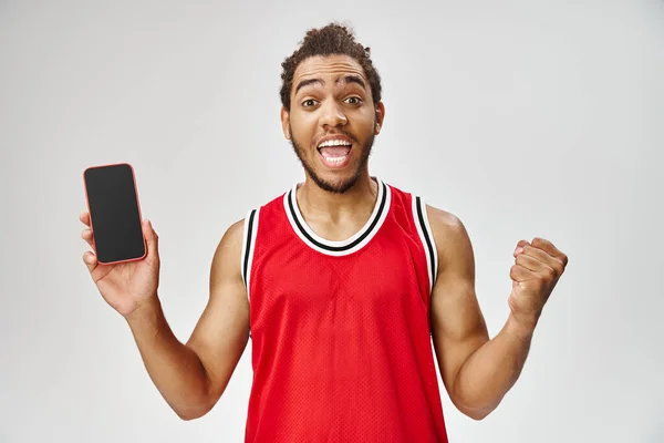 Cheerful african american man in sportwear holding phone and looking at camera, online betting — Stock Photo