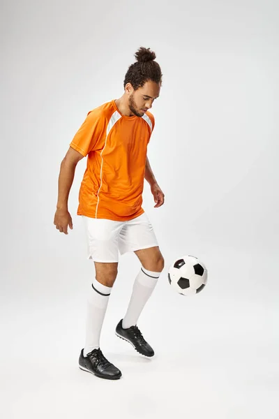 Good looking athletic african american man in sportwear playing football actively on gray backdrop — Stock Photo