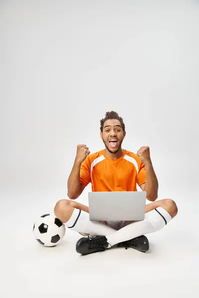 Merry african american sportsman next to football with laptop looking at camera, online betting — Stock Photo