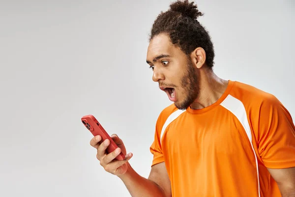 Sorprendido hombre afroamericano en ropa deportiva mirando a su teléfono inteligente, concepto de apuestas en línea - foto de stock