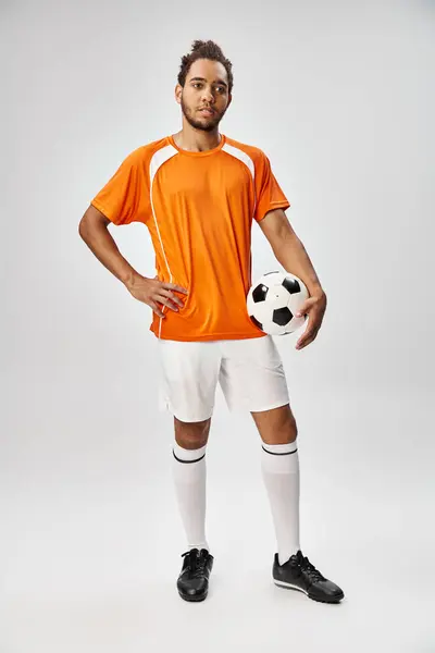 Handsome young african american man in vibrant uniform posing with football on gray background — Stock Photo