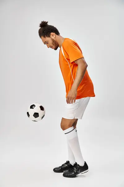 Good looking young african american man in vibrant sportwear playing football on gray background — Stock Photo