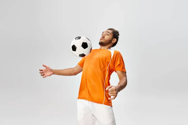Attractive young african american man in sportwear playing football actively on gray background — Stock Photo