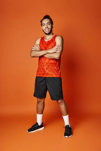 Alegre guapo afroamericano hombre en ropa deportiva posando con los brazos cruzados y mirando a la cámara — Stock Photo