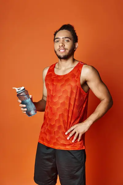 Привабливий веселий афроамериканський чоловік у спортивному одязі, що тримає пляшку води і дивиться на камеру — стокове фото