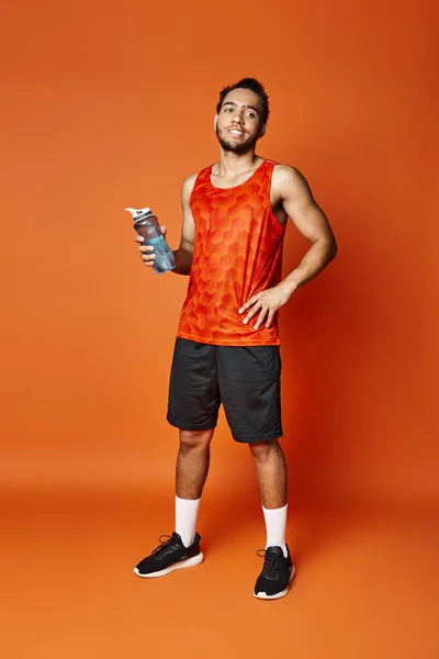 Handsome athletic african american man in vivid sportwear holding water bottle and looking away — Stock Photo