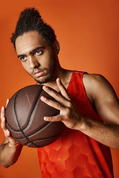 Appealing athletic african american sportsman holding basketball on vibrant orange background — Stock Photo