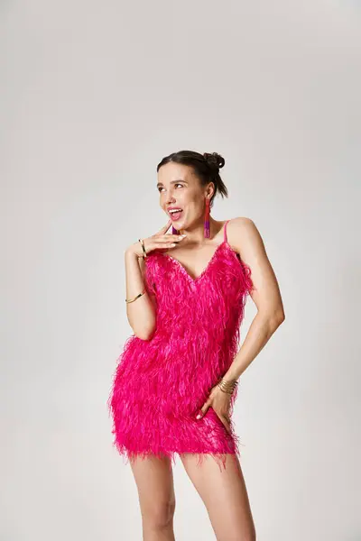 Smiling woman in trendy pink feather dress looking away and touching cheek with finger — Stock Photo