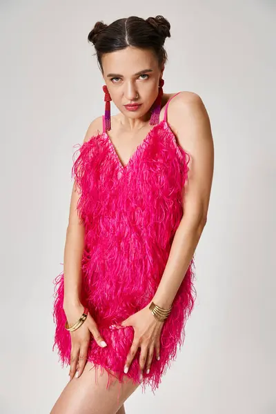 Mujer morena radiante en traje de plumas rosa sosteniendo su vestido y mirando a la cámara con confianza - foto de stock