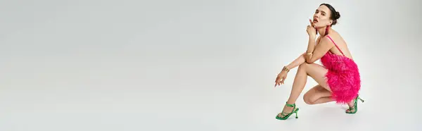 Femme brune en tenue rose regarde calmement et touchant son menton, photo pleine longueur, bannière — Photo de stock