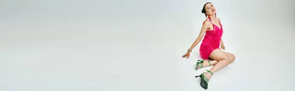 Mujer joven atractiva en elegante vestido rosa mira suavemente, retrato de cuerpo entero sobre fondo gris, pancarta - foto de stock